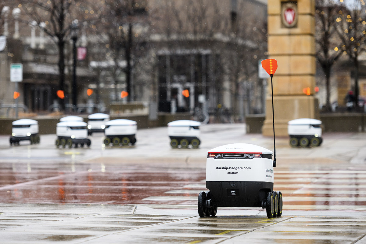 A line of food delivery robots wait to cross a street
