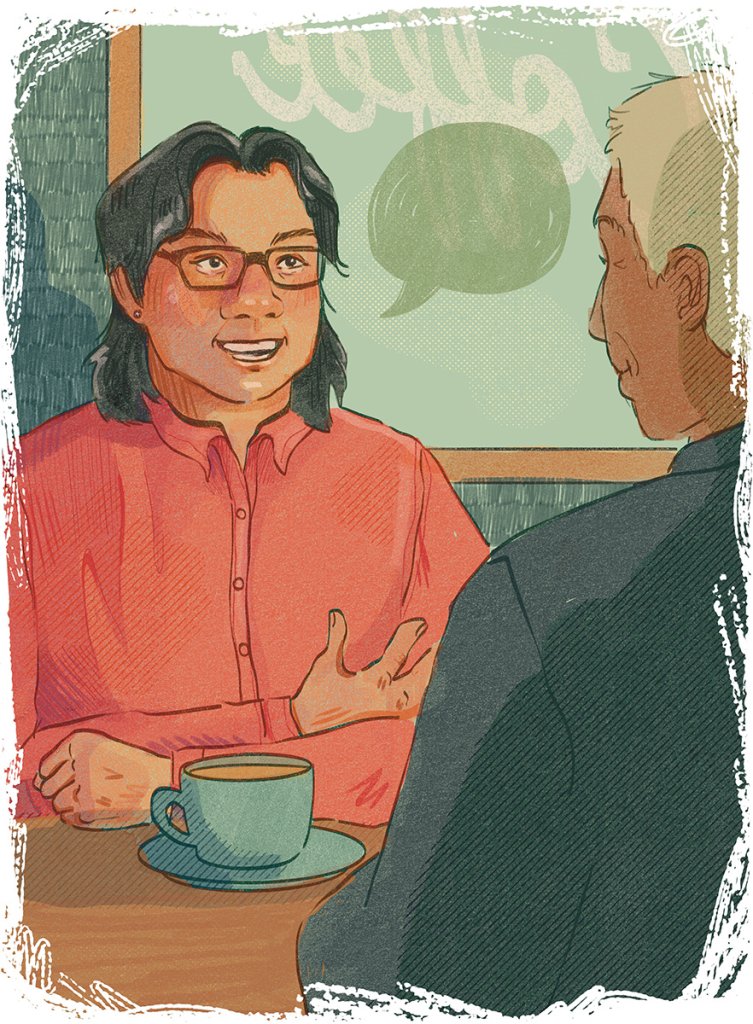 Two people sit across from each other at a table, one in a red shirt gesturing with one hand while the other listens attentively, with a cup and saucer on the table.