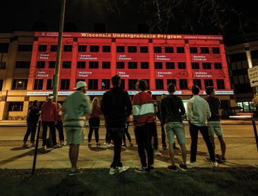 Students line up to watch nighttime display of congratulatory messages for graduates projected on the side of Grainger Hall