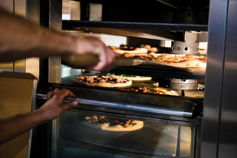 Chef at Ian's loads pizzas into a large oven