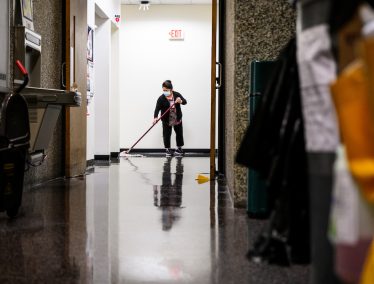 Custodial staff mops floor in lobby of office building