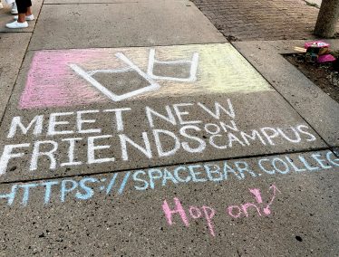 Sidewalk chalk writing reads, "Meet new friends on campus"