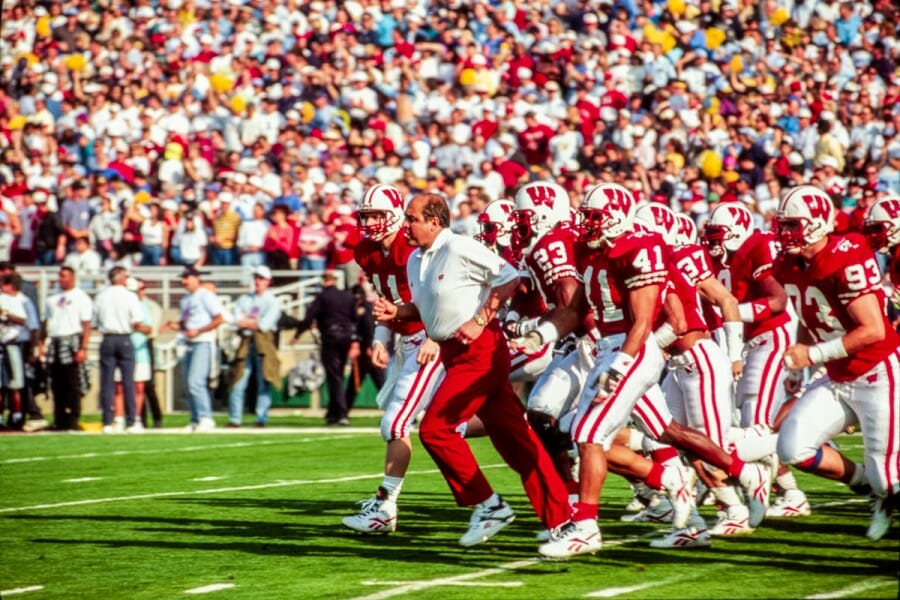 Barry Alvarez runs across field with Badger football team during the 1994 Rose Bowl game