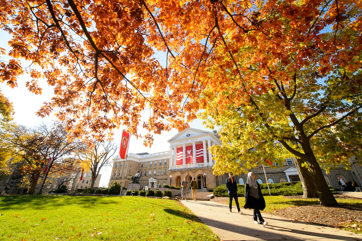Students walk along a colorful tree-lined sidewalk outside Bascom Hall in fall 