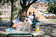 Student wearing face mask works on laptop outside