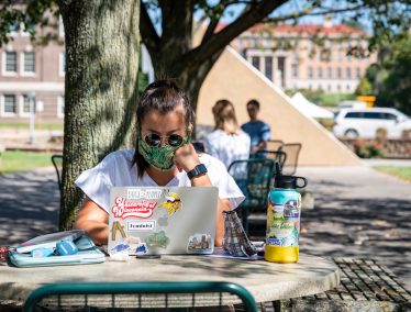 Student wearing face mask works on laptop outside