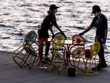 Wisconsin Union staff clean and sanitize tables and sunburst-designed chairs in between patrons enjoying physically distanced, reserved-table seating with food and drink service at the Memorial Union Terrace