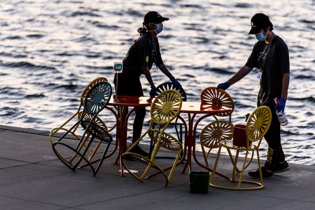 Wisconsin Union staff clean and sanitize tables and sunburst-designed chairs in between patrons enjoying physically distanced, reserved-table seating with food and drink service at the Memorial Union Terrace
