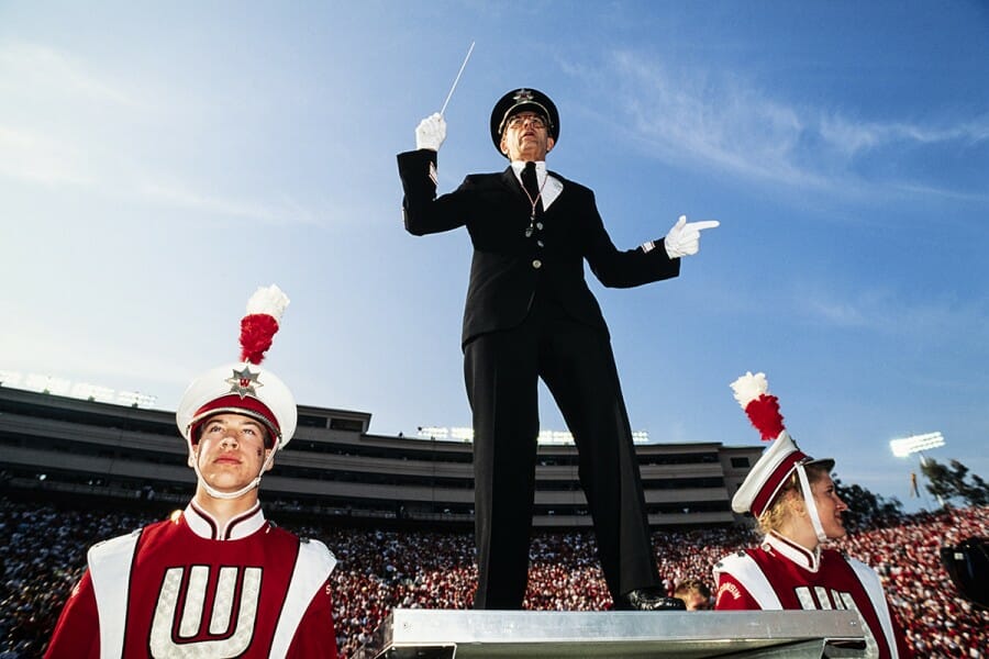 1994 photo of Mike Leckrone leading the UW Marching Band flanked by two band members in their uniforms