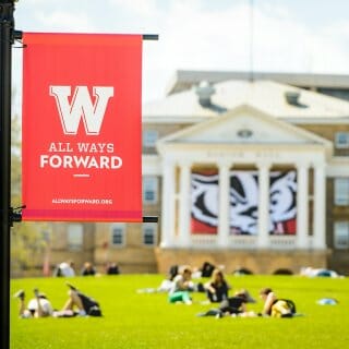 Red Banner shows the All Ways Forward logo, while in the background students lounge on the grass of Bascom Hill