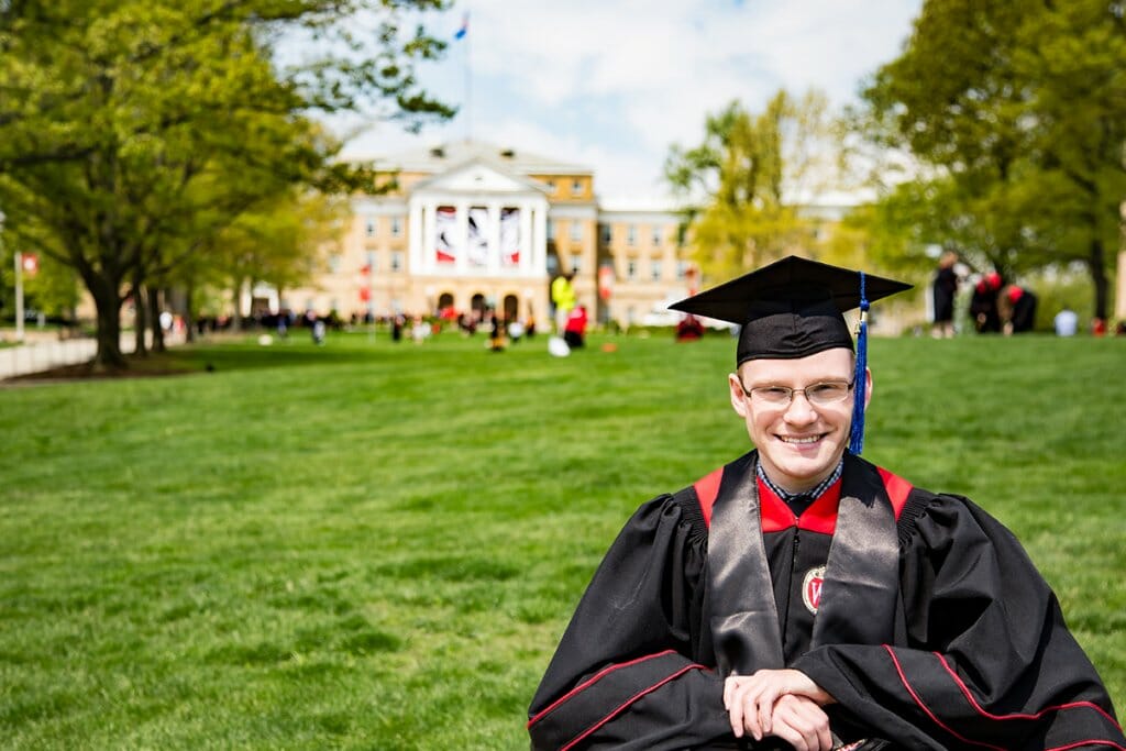 Kramer Endres smiles on Bascom Hill wearing graduation cap and gown