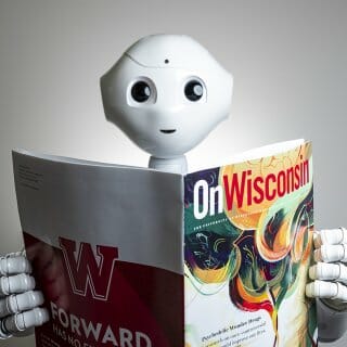 White robot with large bright eyes holds a copy of the On Wisconsin Alumni Magazine