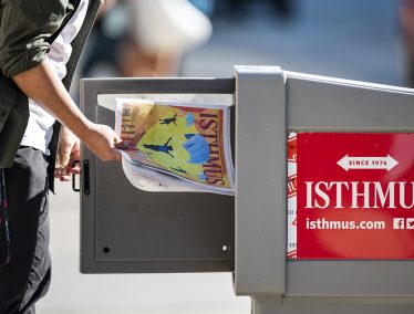 Person takes a copy of the Isthmus newspaper out of a stand on the street