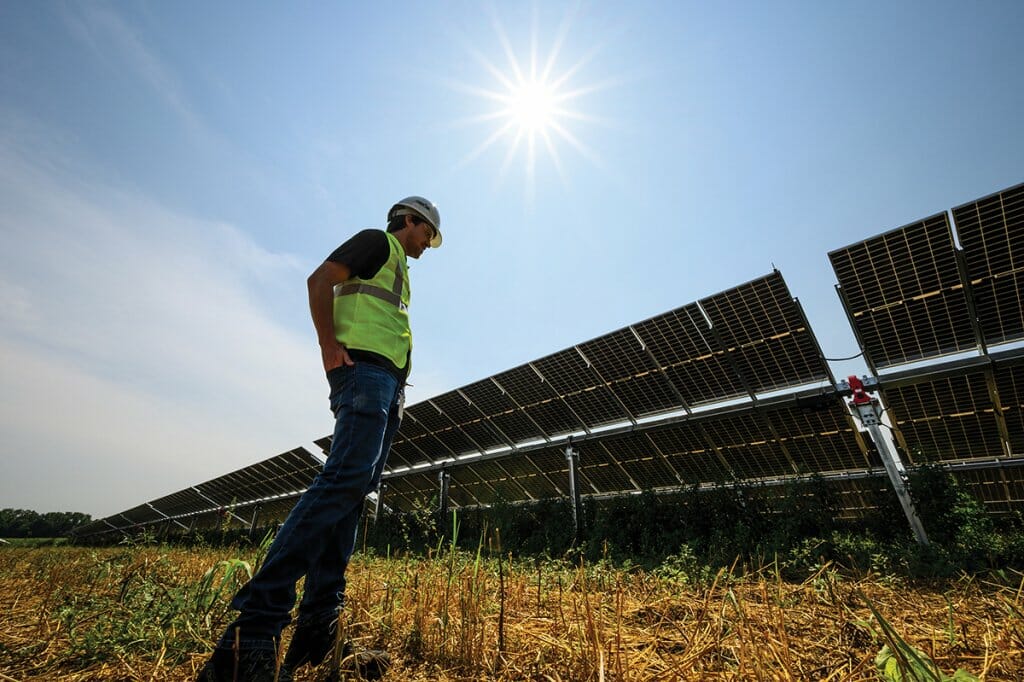 Madison Gas and Electric worker in reflective vest and hard hat stands in front of a row of large solar panels