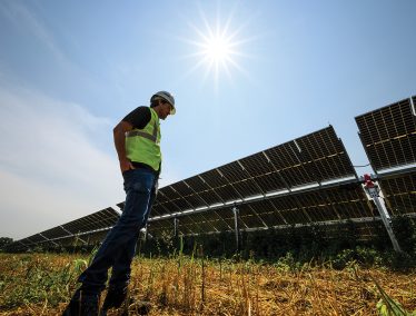 Madison Gas and Electric worker in reflective vest and hard hat stands in front of a row of large solar panels