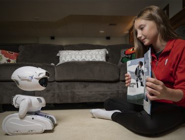 Girl reads book to robot in living room