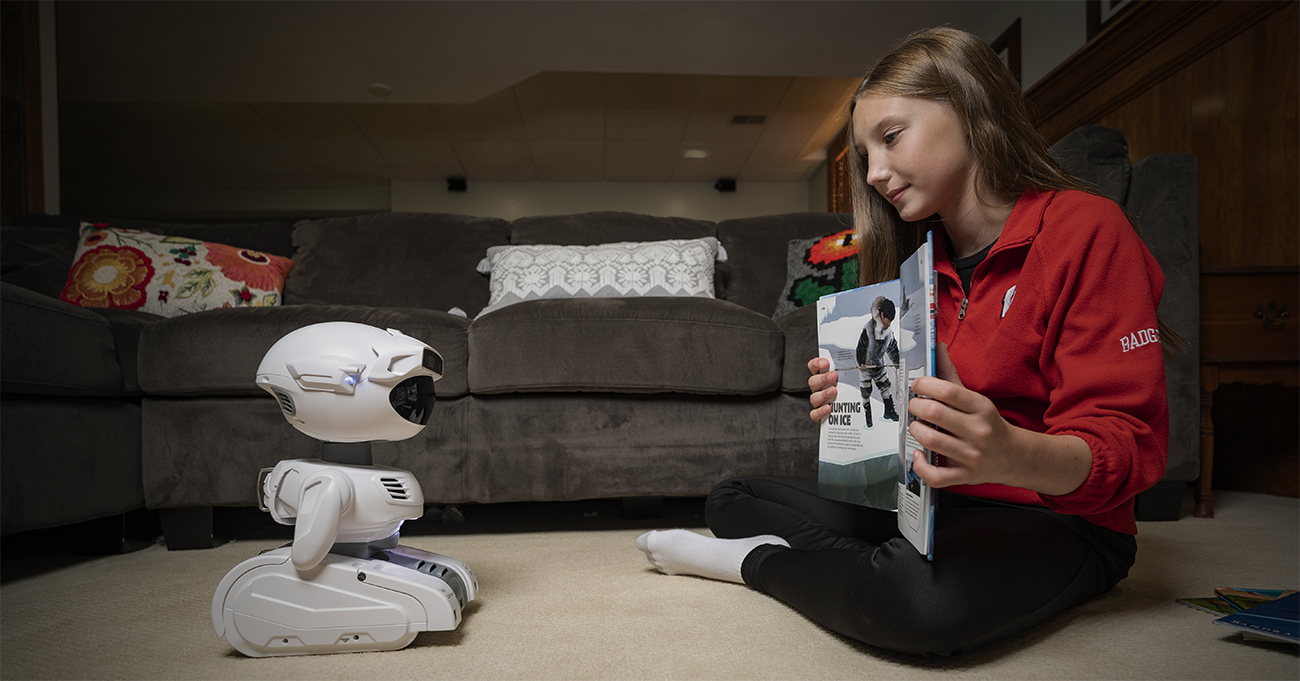 Girl reads book to robot in living room