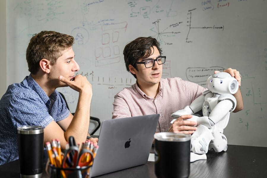 Two researchers examine a small white doll-sized robot.