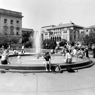 Black and white archival photo of students perched on the edge of the Library Mall fountain