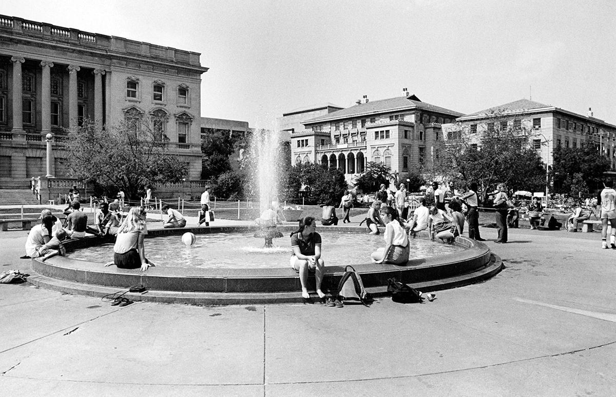 Black and white archival photo of students perched on the edge of the Library Mall fountain