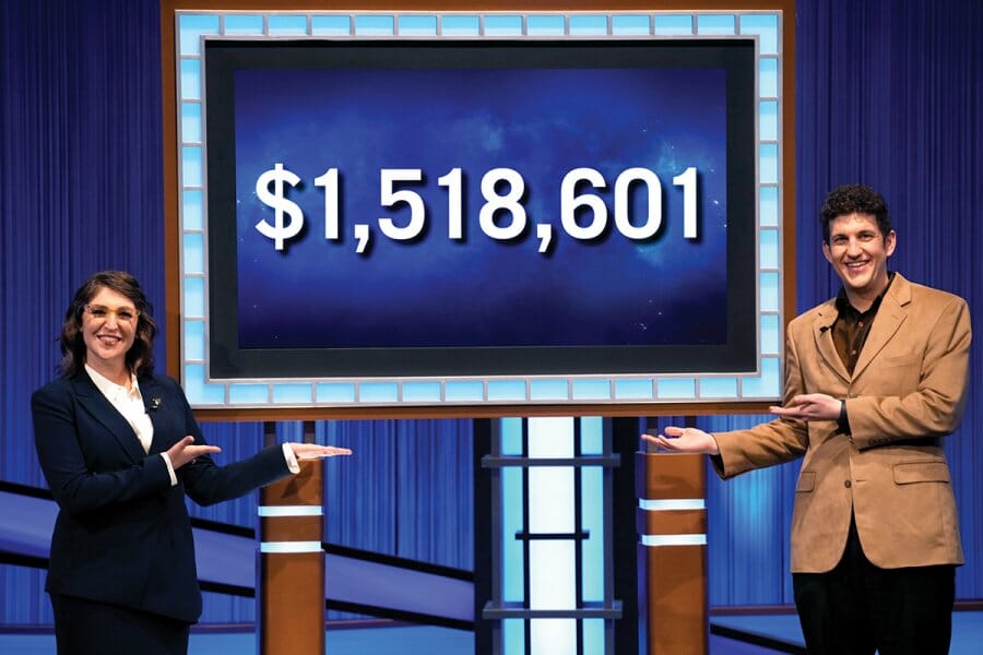 Matt Amodio stands with actress, Mayim Balik, in front of a Jeopardy screen showing the dollar amount $1,518,601