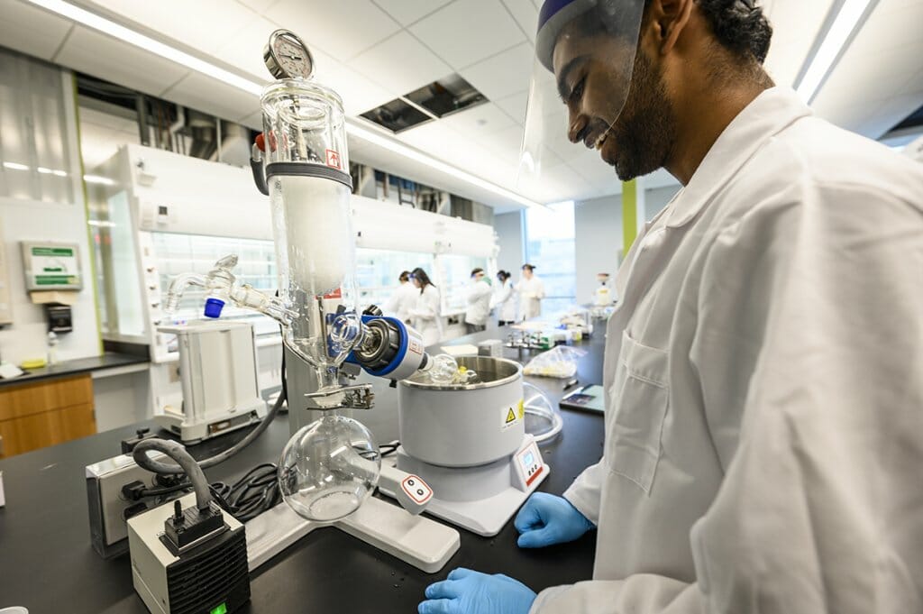 Shrey Ramesh wearing a white lab coat operates a rotary evaporator