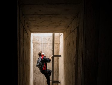 View of the illuminated end of a long dark hallway where On Wisconsin writer Preston Schmitt climbs up a ladder
