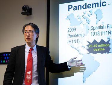 Prof. Yoshihiro Kawaoka gives a talk in front of a projector screen