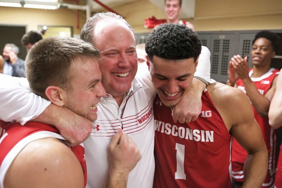 Gard smiles and embraces two Badger basketball players in the locker room