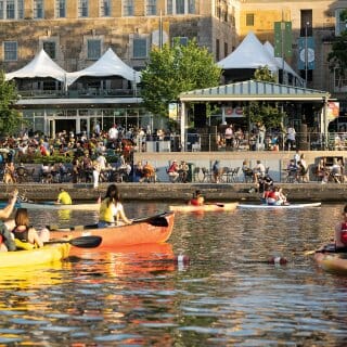 View from Lake Mendota of patrons on the Terrace enjoying early evening sun and live music with colorful canoes in the foreground