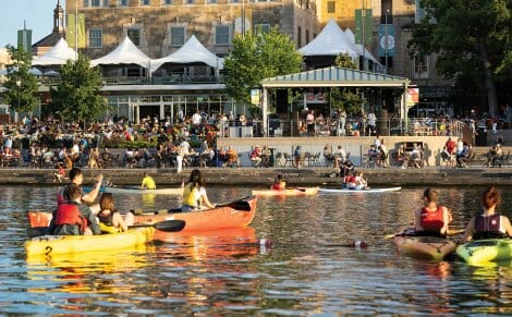 View from Lake Mendota of patrons on the Terrace enjoying early evening sun and live music with colorful canoes in the foreground