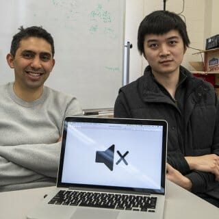 Fawaz and Yang pose together with a laptop displaying a large mute button