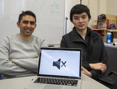 Fawaz and Yang pose together with a laptop displaying a large mute button