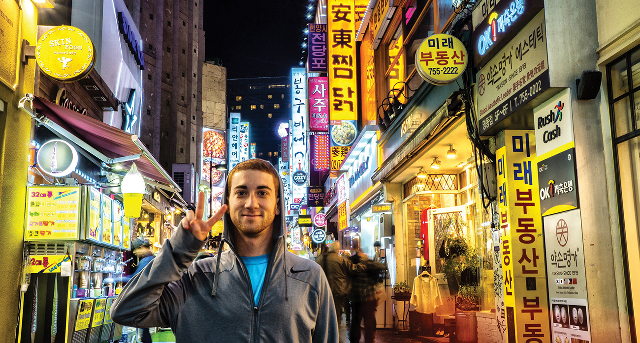 Drew Binsky makes the "peace" sign in the illuminated nighttime downtown area of Seoul, South Korea