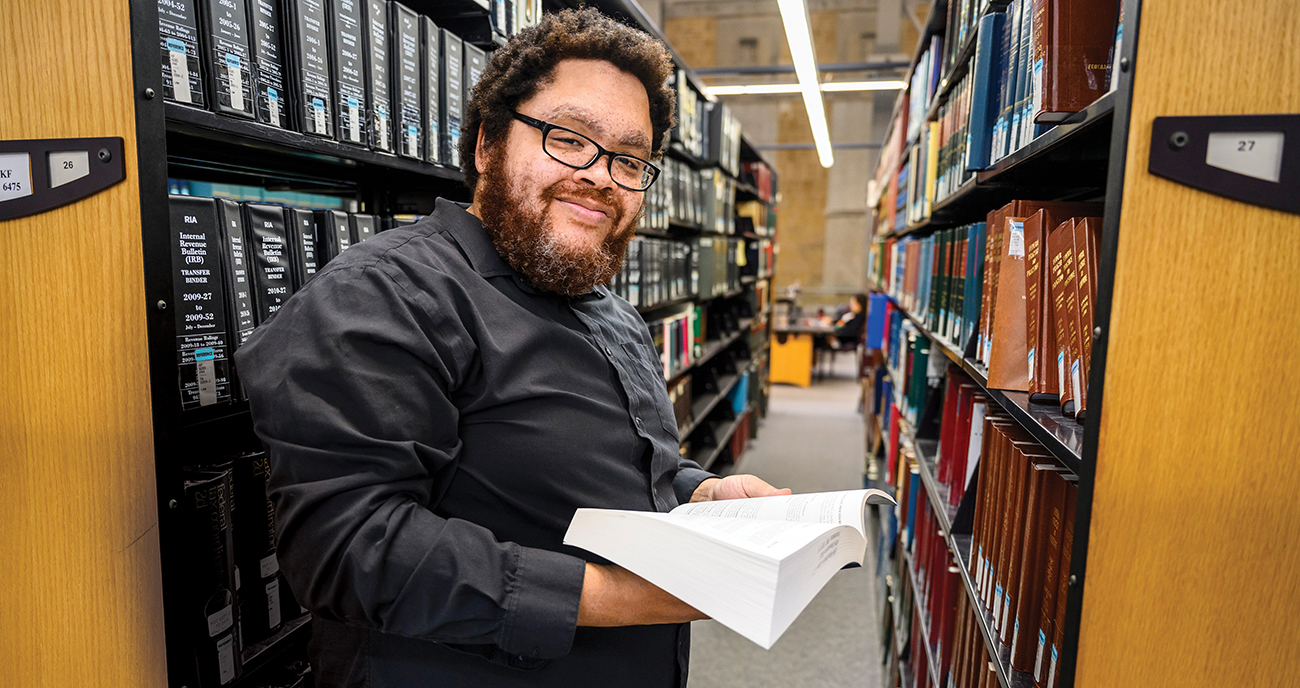 Steven Wright poses with open book in front of library book stacks