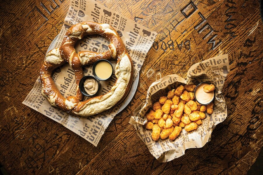 Food baskets containing a soft pretzel and cheese curds sit atop a Rathskeller table covered with student graffiti carvings