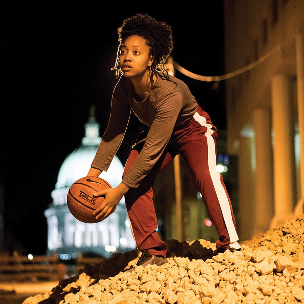 Zhararina Sanders holding a basketball at night with the glow of the Wisconsin State capitol dome in the background