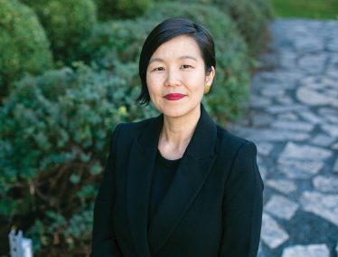 Monica Kim wearing black against a background of green foliage