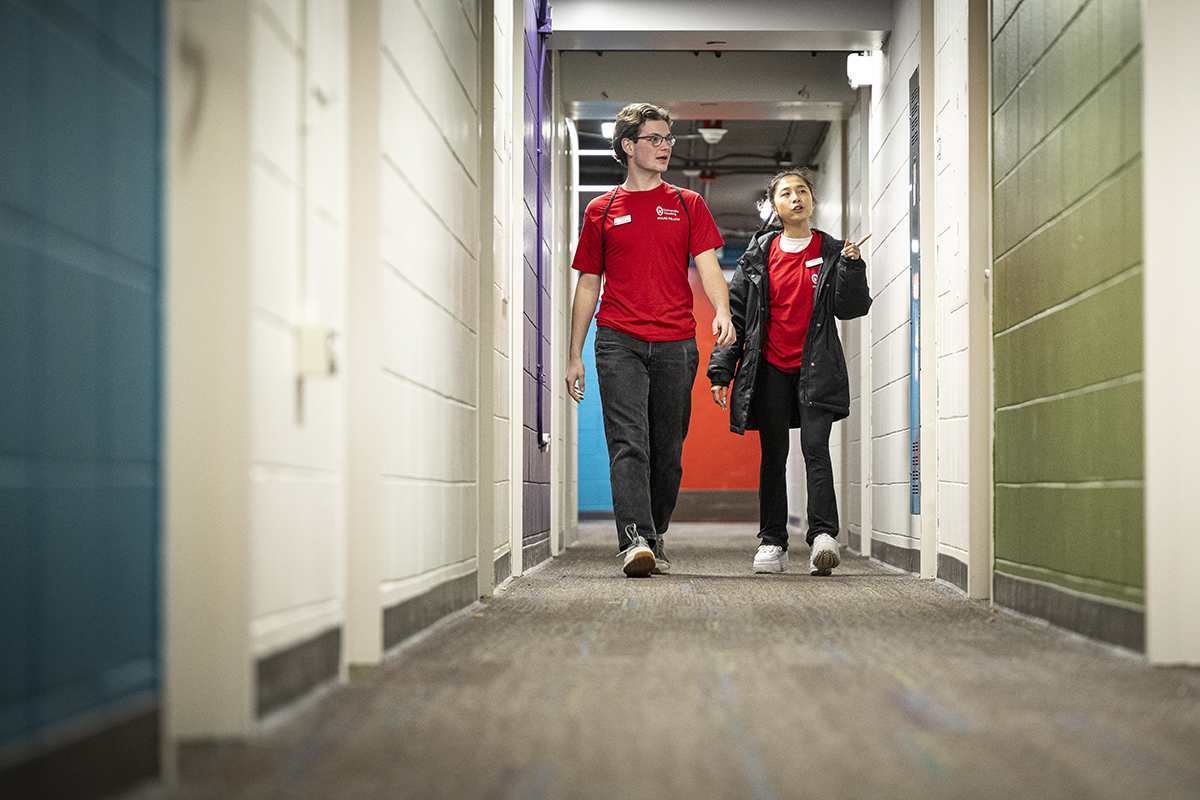 Two house fellows dressed in red shirts converse as they walk down a dormitory hallway