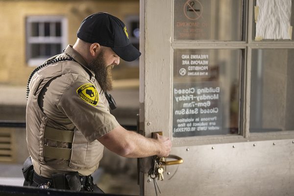 Kyle Kaul wearing a security uniform locks a door with a large set of keys