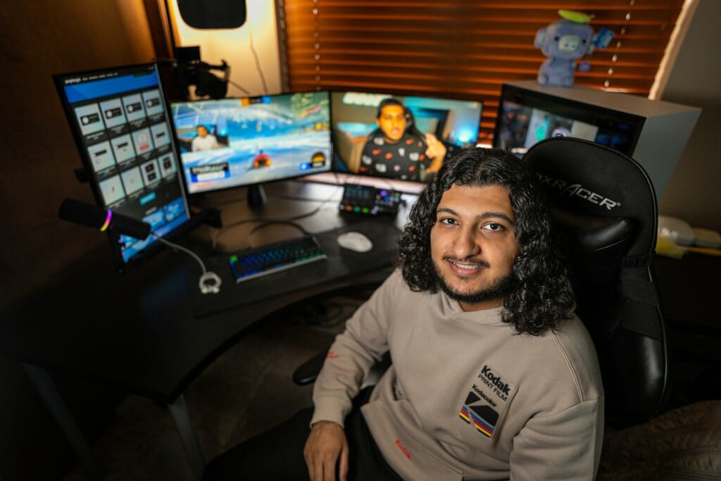 Muaaz Shakeel is seated at a computer desk with multiple monitors.