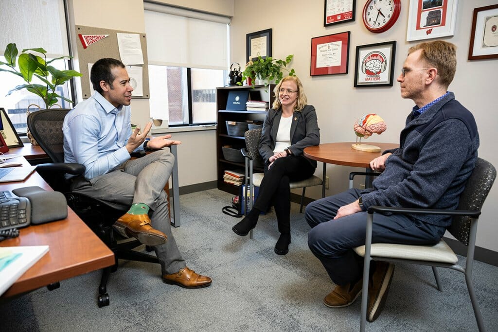 Nate Chin, gesturing, Cynthia Carlsson and Sterling Johnson having a discussion in an office at University Hospital. 