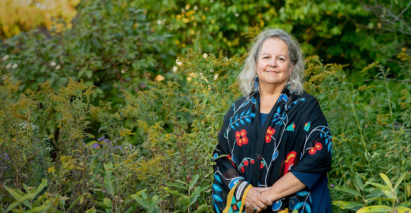 Robin Wall Kimmerer stands in the middle of a lush green outdoor area