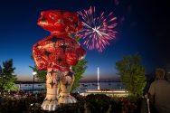 Red and white Bucky Badger statue stands against a dusky sky lit by fireworks
