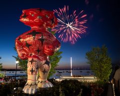 Red and white Bucky Badger statue stands against a dusky sky lit by fireworks