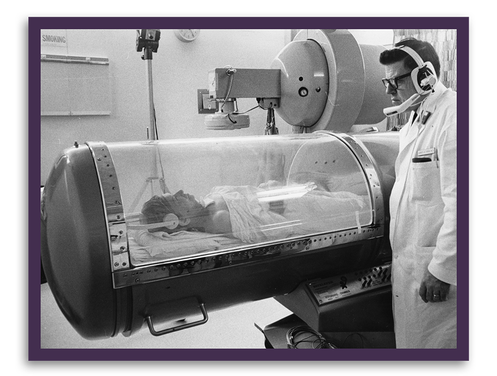 Black and white photo of doctor monitoring person in early MRI machine