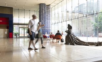 Patrons in the lobby of the Chazen museum which features floor to ceiling windows and a large bronze statue.