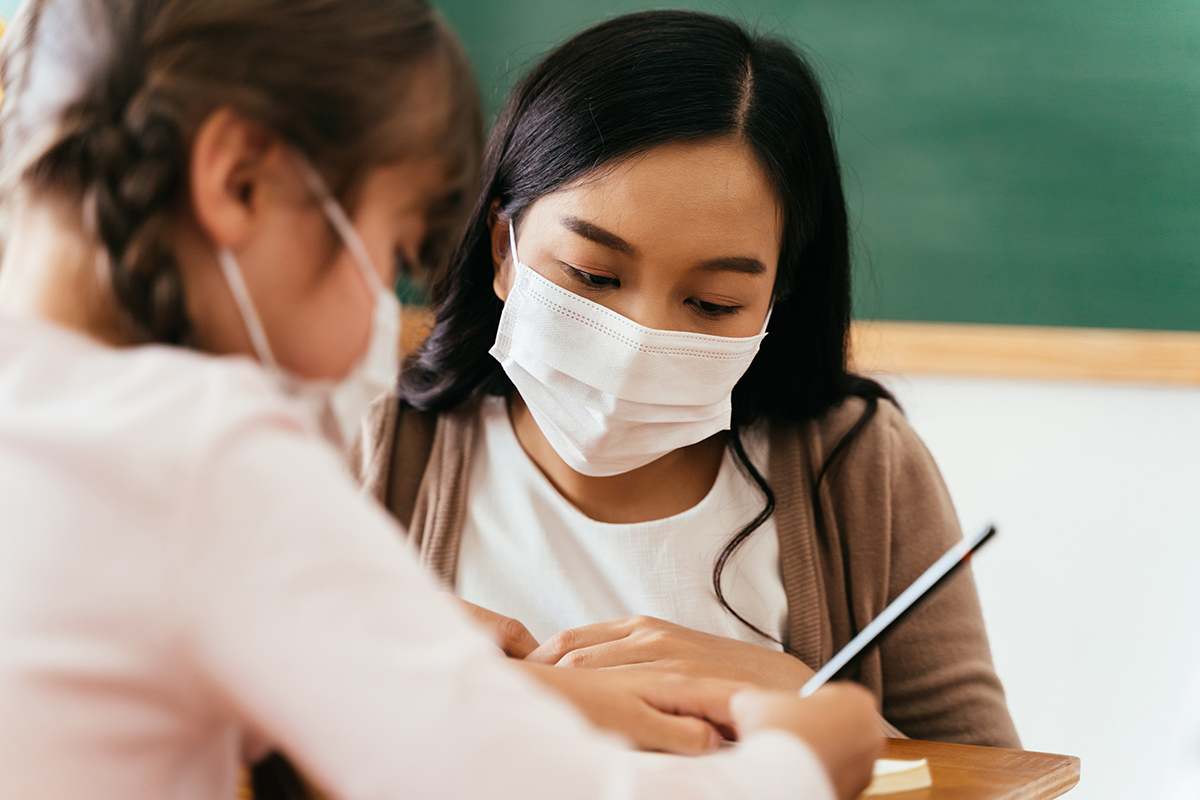 Teacher works with student while both wear masks
