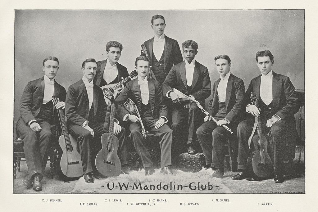 Black and white image showing a group of eight men, most seated, with their mandolins.