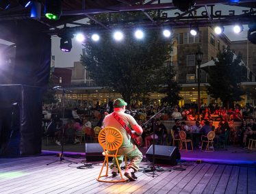 A guitarist sits facing the audience on the Union Terrace stage